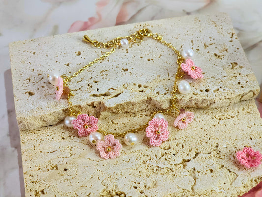 Handcrafted micro-crochet Sakura blossoms flanked by natural 5-6mm freshwater pearls on an 14K gold-plated bracelet close up.