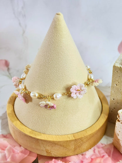 Handcrafted pink-white micro‑crochet Sakura blossoms, flanked by 5-6mm natural Baroque pearls. 14K gold-plated bracelet.